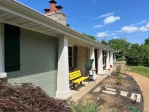Front porch makeover of a St. Louis ranch-style home with sage green painted brick, white columns, and dark green shutters, expertly refinished by Malone Painting