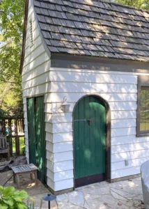 Backyard shed with freshly painted white siding and a vibrant green arched door, showing a custom exterior painting project.