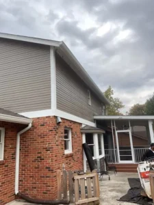 A side view of a two-story brick and siding house with a screened-in porch on the ground floor. White trim separates the brick and brown siding. The sky is cloudy