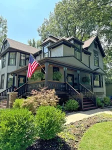 Exterior painting on a historic two-story house with light gray siding and dark brown trim, showcasing intricate details and railings.