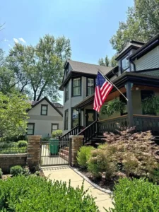 Exterior painting on a historic two-story house, showcasing the new light gray siding and dark brown trim around the porch and windows.