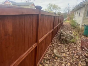 Completed fence staining project, showing a restored wooden fence with a fresh, dark stain.