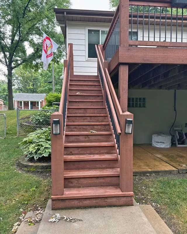 Deck and railing refinishing service, showing the top of a set of stairs with a faded reddish-brown stain.
