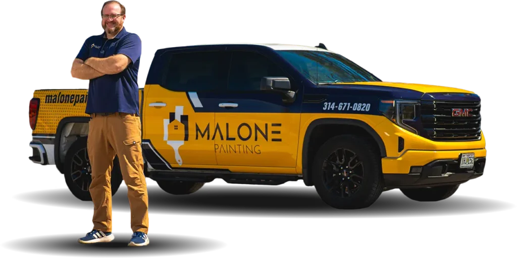 Jack, one of the Production Managers at Malone Painting, stands with his arms crossed next to a branded yellow and blue company truck. The background is transparent