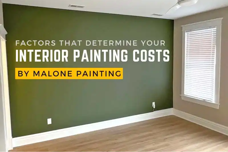 A wide shot of a living room with one accent wall painted a dark green and the other walls painted a beige color. The floors are a light wood laminate, and a white ceiling fan hangs from the ceiling. White overlay text reads "FACTORS THAT DETERMINE YOUR INTERIOR PAINTING COSTS" with "BY MALONE PAINTING" in a yellow box.
